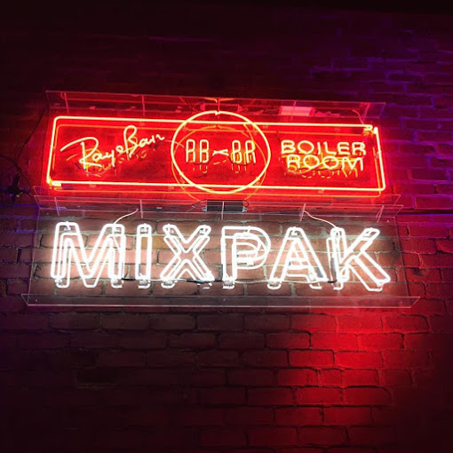 "Neon signs for Ray-Ban Boiler Room and Mixpak on brick wall."