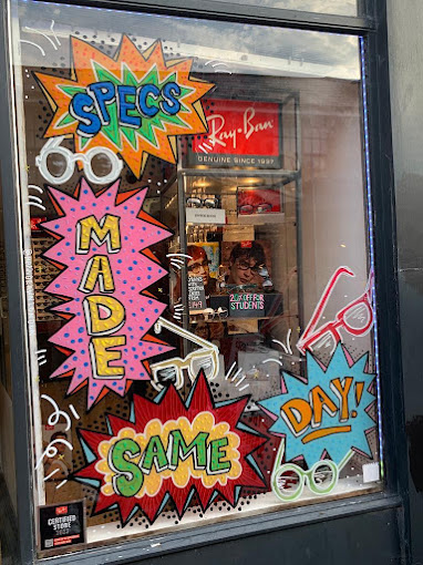 "Eyewear shop window with vibrant 'Specs Made Same Day' graphic."