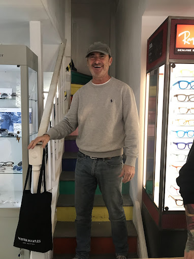 "Man smiling, standing inside eyewear shop next to colorful staircase."