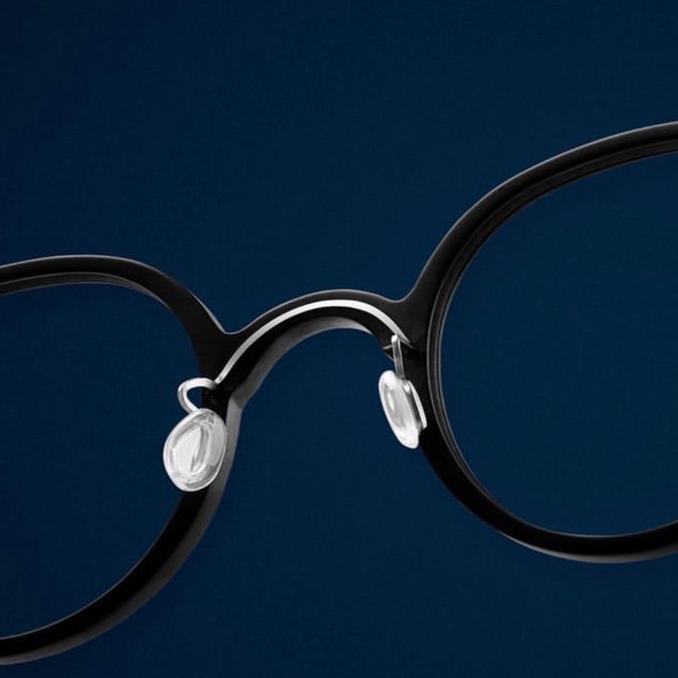 "Minimalist close-up of round eyeglasses with nose pads on dark background."